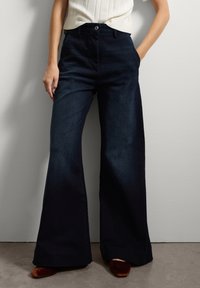 Donkerblauwe wijde broek met een hoge taille, voorzien van twee zijzakken, een knoopsluiting en een subtiele denimtextuur.
