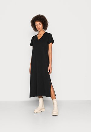 Svart kortärmad klänning med V-ringning, med sidoklipp. Modellen matchar den med krämfärgade ankelstövlar. Slät, lätt material.