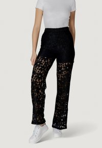 I pantaloni neri in pizzo presentano un motivo floreale, un tessuto semitrasparente, una vita alta e una vestibilità slim. Indossati con sneakers bianche per creare un contrasto.