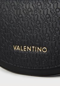 Borsa a tracolla in pelle nera con motivo in rilievo del logo "VALENTINO" e dettagli in oro. Texture liscia con forma strutturata.