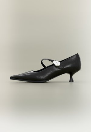 Chaussure Mary Jane en cuir noir avec bout pointu, petit talon kitten incurvé et boucle ovale argentée sur la bride, vue de profil.