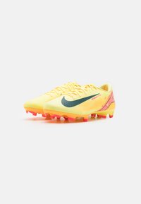Kollased jalgpallijalatsid tekstureeritud pealsiga, millel on must swoosh ja roosad aktsendid külgedel ning punaste otstega nupukesed haardeks.