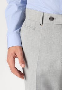 Pantalon texturé gris clair avec une taille ajustée, doté d'une fermeture à bouton et d'une poche latérale. Associé à une chemise bleu clair aux poignets.