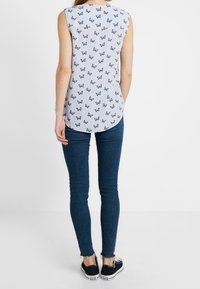 Ärmlös topp med vertikala blå och vita ränder, prydd med ett fjärilsmönster. Matchas med mörka slim fit jeans och svarta sneakers.