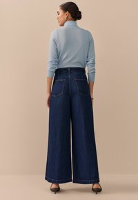 Wijde donkerblauwe denim jeans met een hoge taille, gecombineerd met een lichtblauw shirt met lange mouwen. Heeft achterzakken en een schone afwerking.
