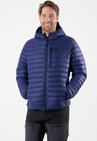 Marineblauwe gewatteerde jas met capuchon, met zigzagstiksels, voorrits en twee zijzakken. Gelaagd, gepadded materiaal.