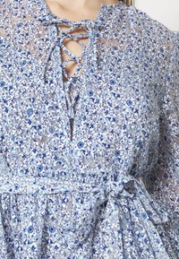 Gros plan d'une robe fleurie bleue avec un col lacé en croix et une ceinture en tissu nouée à la taille.