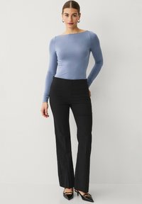 Top azul claro de manga larga con escote barco, combinado con pantalones acampanados negros de cintura alta. El conjunto presenta un diseño elegante y ajustado.