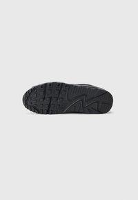 Talpa de adidasi negri, cu cauciuc texturat, având un model de striații pentru aderență și un logo Nike pronunțat pe lateral.
