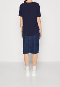 Námořnické tričko s krátkým rukávem spárované s modrou džínovou midi sukní se zřaseným lemem. Nošeno s bílými ponožkami a robustními teniskami.