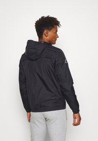 Schwarze, leichte Jacke mit Kapuze, elastischen Bündchen und Saum. Der Stoff wirkt glatt und glänzend. Verfügt über ein Logodetail auf der linken Schulter.