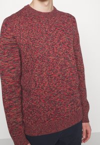 Maglione in maglia con un motivo mélange texturizzato di rosso e grigio. Collo a giro, polsini e orlo a costine, silhouette aderente.