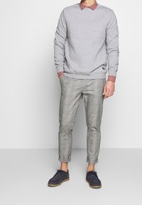 Sweat-shirt matelassé gris avec un col bordeaux, associé à un pantalon à carreaux gris. Complété par des chaussures bleu marine. Présentation d'une tenue décontractée.