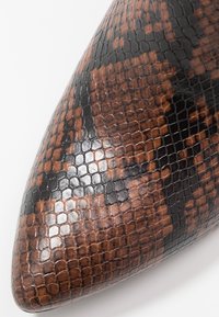 Chaussure à bout pointu arborant un motif texturé de peau de serpent noir et marron. Finition brillante avec une variation subtile de couleur pour plus de détails.