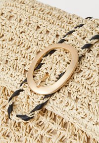 Vævet strå clutch-taske i beige med et struktureret mønster, sort snoet håndtag og en guldfarvet oval spænde detalje.