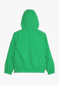 Zielona kurtka z kapturem wykonana z lekkiego, teksturowanego materiału. Posiada elastyczne mankiety i ściągacz na dole. Gładki widok z tyłu.