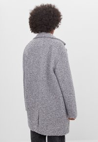 Abrigo gris claro hecho de tejido texturizado con un corte holgado, gran cuello y abertura en la parte posterior, con mangas largas y un diseño de longitud media.