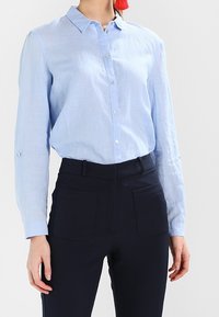 Camicia azzurro chiaro in misto lino, con colletto classico e maniche lunghe, abbinata a pantaloni blu scuro con tasche frontali.