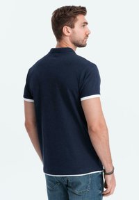 Námořnická modrá polo košile s krátkým rukávem, bílým límcem a akcenty na rukávech. Bavlněný materiál, čistý design a uvolněný střih.