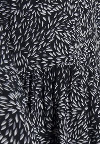 Czarna tkanina z rozproszonym wzorem liści w kolorze białym z jasnoszarymi akcentami; zawiera zebrane tekstury w szwie.