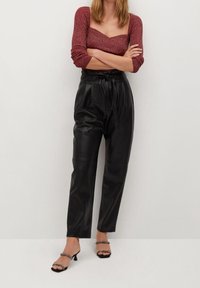 Pantalon taille haute en cuir noir avec des détails plissés à l'avant, associé à un haut ajusté à manches longues rouge et des talons noirs à lanières.
