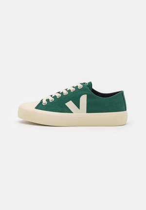 Baskets basses en toile verte avec lacets blancs, semelle crème, bout renforcé et logo blanc "V" sur le côté.