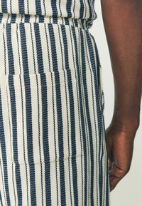 Pantalons rayés avec des lignes alternant bleu marine et crème, dotés d'une poche plaquée sur le côté et d'une finition en tissu texturé.