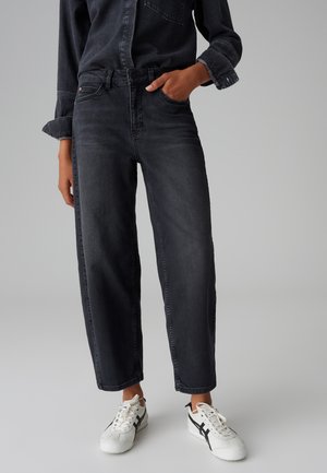Schwarze High-Waist-Jeans mit geradem Bein, ausgestattet mit frontalen Taschen, einem Knopfverschluss und minimalen Ausbleichungen. Getragen mit weißen Sneakers.