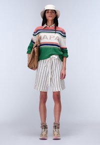 Kleurrijke gestreepte gebreide trui met 'NAPA' tekst, gecombineerd met beige gestreepte shorts en lichte sneakers. Draagt een tan tote bag.