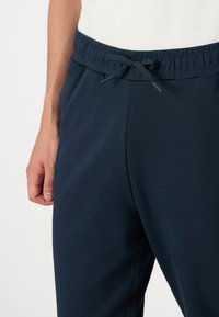 Mørkeblå sweatpants har en elastisk talje med snøre, sidesømme og en blød, glat stofstruktur.