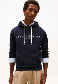 Sudadera con capucha azul marino hecha de mezcla de algodón, con bolsillo tipo canguro, capucha con cordón y logo bordado con detalles en rojo y azul.