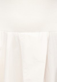 Υφασμα εκρού με λεπτομέρεια ραφής που συγκεντρώνεται, δείχνοντας αντίθεση υφής μεταξύ λείου και πλεγμένου υλικού.