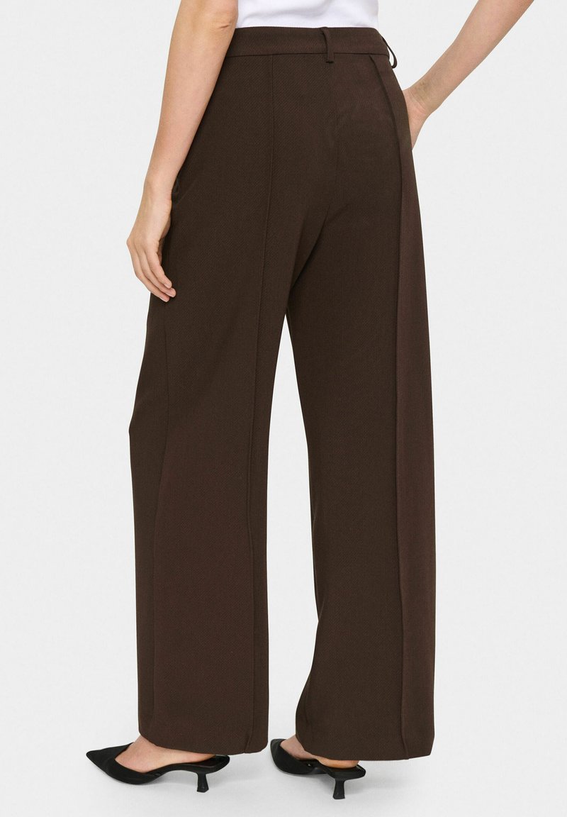 Brązowe spodnie o szerokich nogawkach o gładkiej fakturze, z płaskim paskiem w talii i bocznymi kieszeniami. Noszone z czarnymi szpilkami z ostrym noskiem.