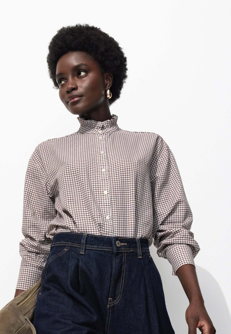 Chemise à carreaux à col volant en crème, rouge et bleu, assortie à un jean en denim foncé taille haute et un sac beige.