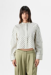 Randig, kort blus i grädde med svarta vertikala linjer, med hög halsringning, långa ärmar och en knappstängning fram.