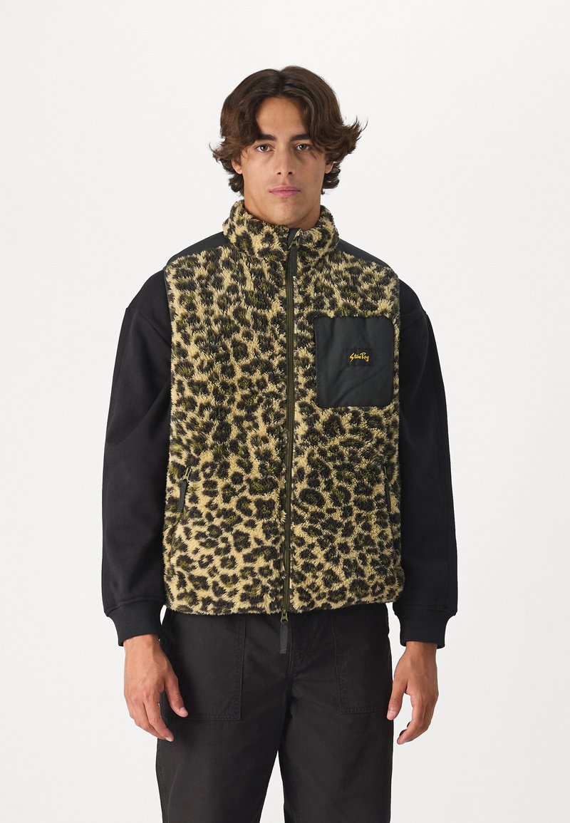 Fleeceová vesta s leopardím vzorom v béžovej a čiernej farbe, má predný zips a čiernu vrecko s žltým logom. Čierne rukávy a robustná textura.