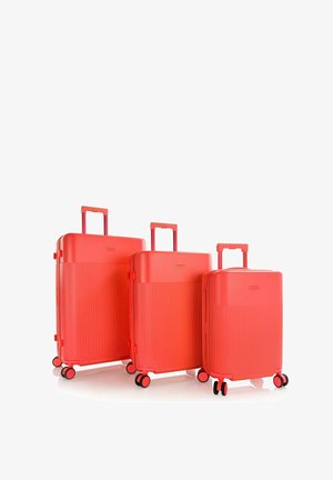 Drei rote Hartschalenkoffer unterschiedlicher Größe mit ausgezogenen Griffen und jeweils vier doppelten Rollen, nebeneinander angeordnet.