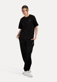 Svart sweatshirt och sweatpants-set med lös passform, mjuk textur och diskreta logodetaljer. Kombineras med vita träningsskor.