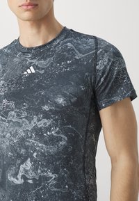 Svart trenings T-skjorte med marmorerte grå mønstre, korte ermer, rund hals og sydd detaljer. Adidas-logo i hvitt på brystet.