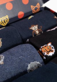 Set di tre calzini di cotone in colori scuri con motivi animali: scimmia, leone e pecora. Confezionati in una scatola decorativa con pois arancioni.