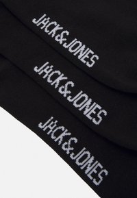 Sorte sokker med hvid strikket tekst "JHCK&JONES" i en fed, moderne skrifttype. Glat tekstur med en tætsiddende form.