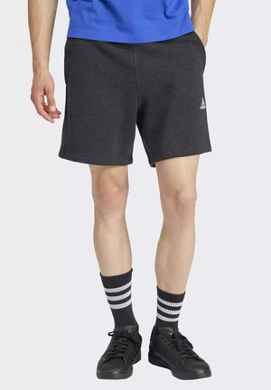 Pantalones cortos deportivos grises con cintura elástica y bolsillos laterales, combinados con zapatillas negras y calcetines a rayas. Diseño simple con acento de logo.
