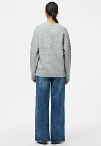 Sivi pleteni pulover sa opuštenim krojem i širokim rukavima, uparen s visokim plavim širokim trapericama, koje imaju mekanu teksturu.