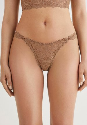 String en dentelle de couleur brun clair, orné de motifs floraux, de bords festonnés et d'une texture délicate. Fins bretelles latérales avec un matériel minimal.