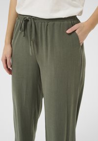 Pantalons de coupe décontractée vert olive en tissu texturé, avec une taille élastique et un cordon de serrage ajustable. présentant des poches latérales et un design de jambe ample.
