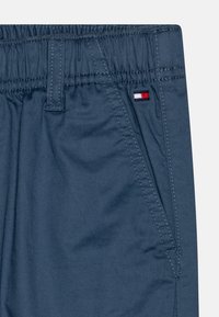 Navyblauwe shorts met een elastische tailleband, voorzien van een gestikt zakje en een klein logo-tag in rood, wit en blauw aan de zijkant.