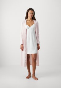 Svetloružový dlhý cardigan cez biele saténové šaty s krajkovými detailmi. Cardigan má textúrovaný, rebrovaný dizajn.