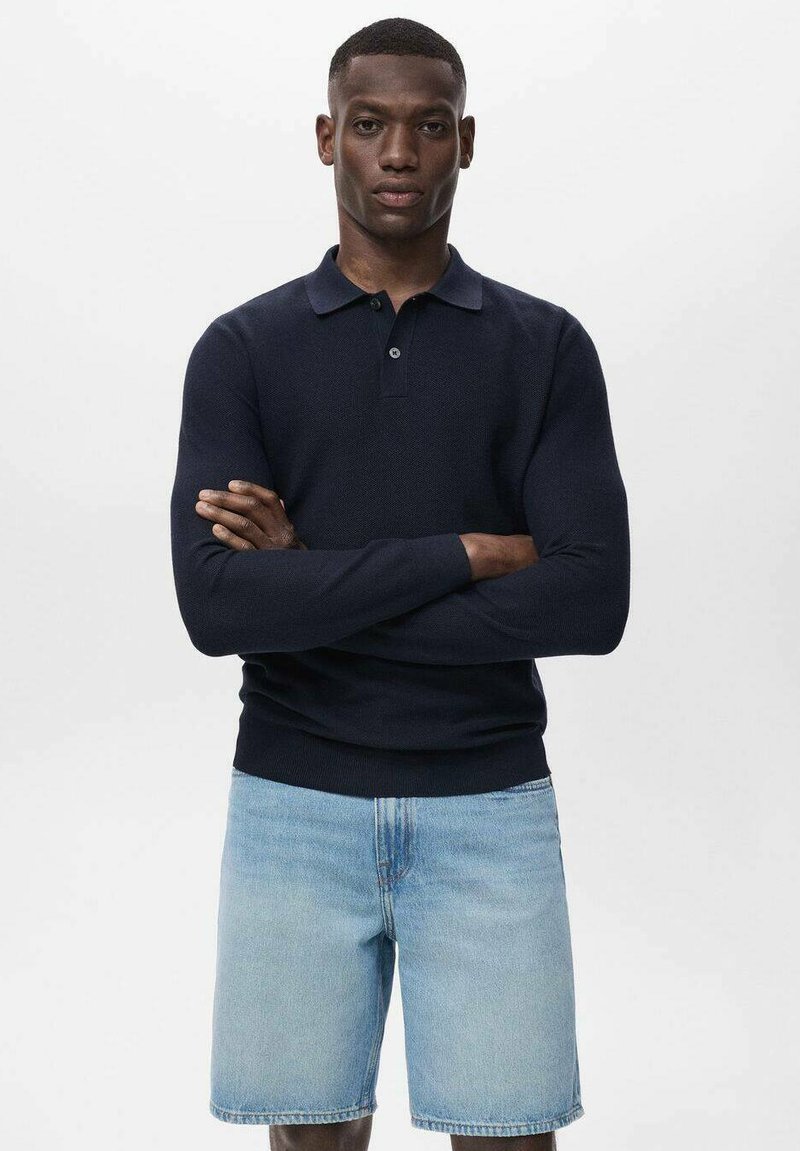 Polo de manga larga en un tono azul marino oscuro con cuello, textura de punto y puños acanalados, combinado con pantalones cortos de mezclilla claros de corte recto.
