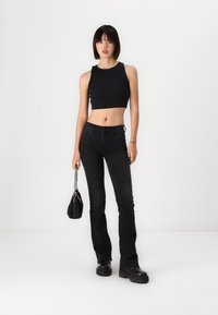 Must have mustarine koonuskaelusega must crop top, millele on sobitatud sobivad mustad laienevad teksad. Riietust täiendab väike must käekott ja rahuldavad mustad jalanõud.