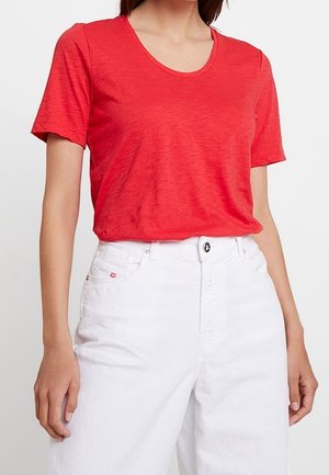 Camiseta roja de manga corta en un tejido suave y texturizado con un escote redondo, combinada con vaqueros blancos de talle alto con cierre de botones.